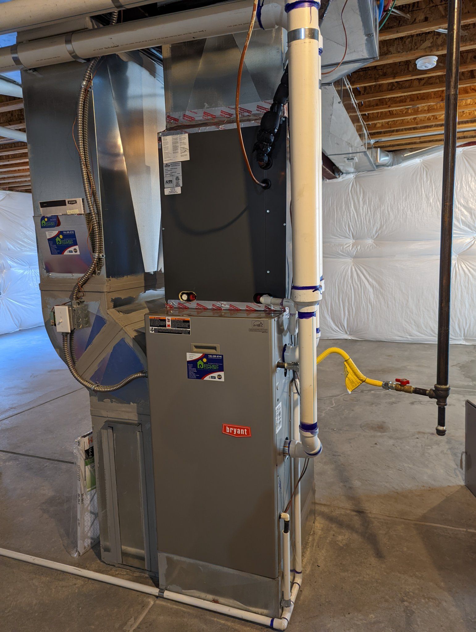 Furnace in a basement, with metal ductwork, and PVC pipes. Gray and silver colors.