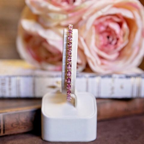 Pink jeweled bracelet displayed on a white stand with blurred pink roses in the background