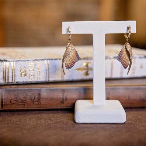 Gold leaf earrings displayed on a white stand with stacked books in the background