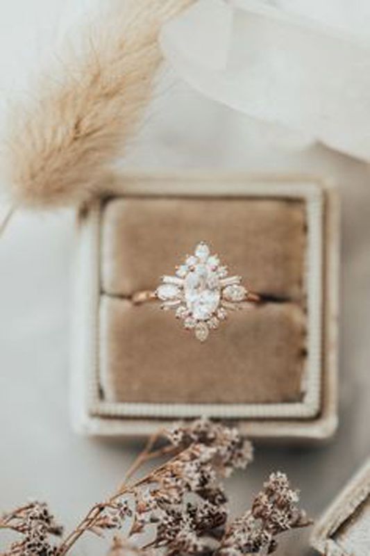 Rose gold ring with a marquise gemstone in a beige velvet jewelry box, surrounded by dried flowers