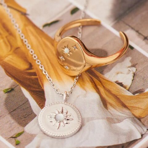 Gold ring and silver sun pendant necklace on a floral fabric background