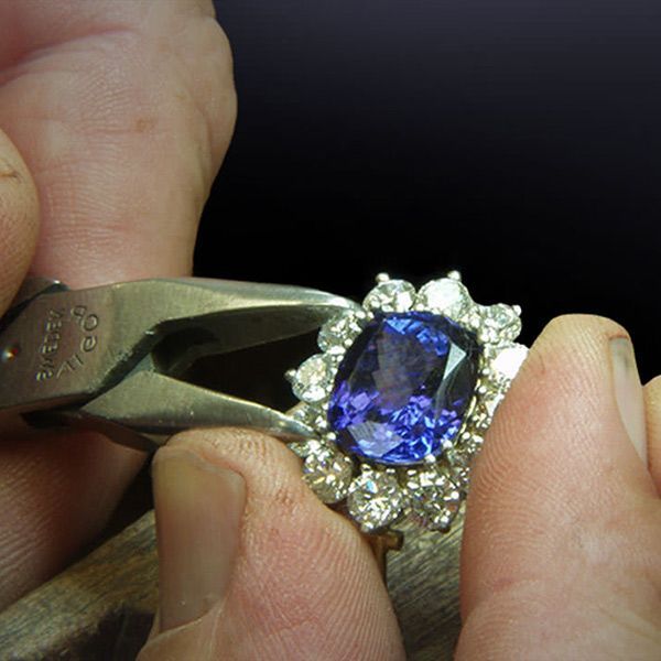 Hand holding a diamond ring with a blue oval gemstone and halo setting