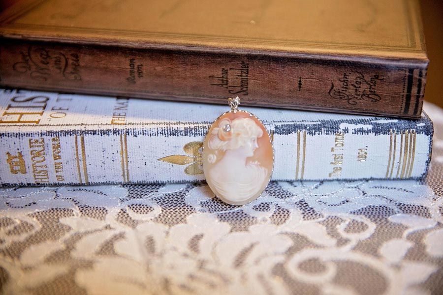 Stacked vintage books with an oval pendant resting on top, on a lace tablecloth