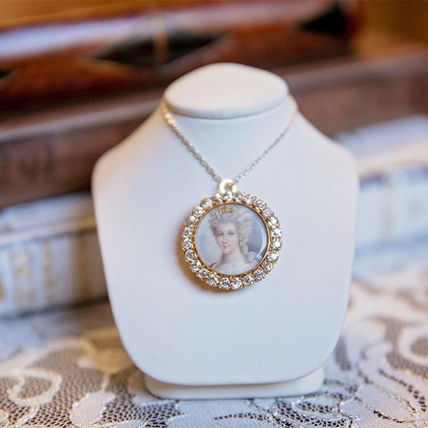 White jewelry bust displaying a gold locket necklace with a small portrait pendant on lace