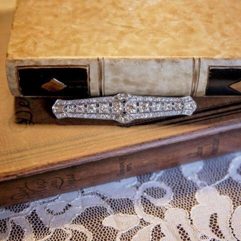 Diamond-studded brooch on a wooden desk beside lace fabric