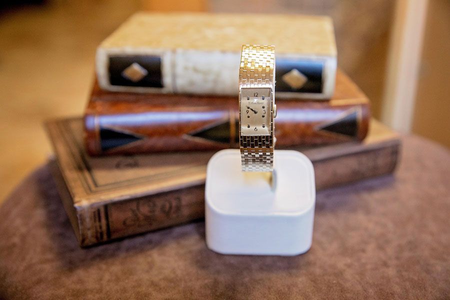 Gold watch on white stand with wooden bands stacked behind it on a brown surface
