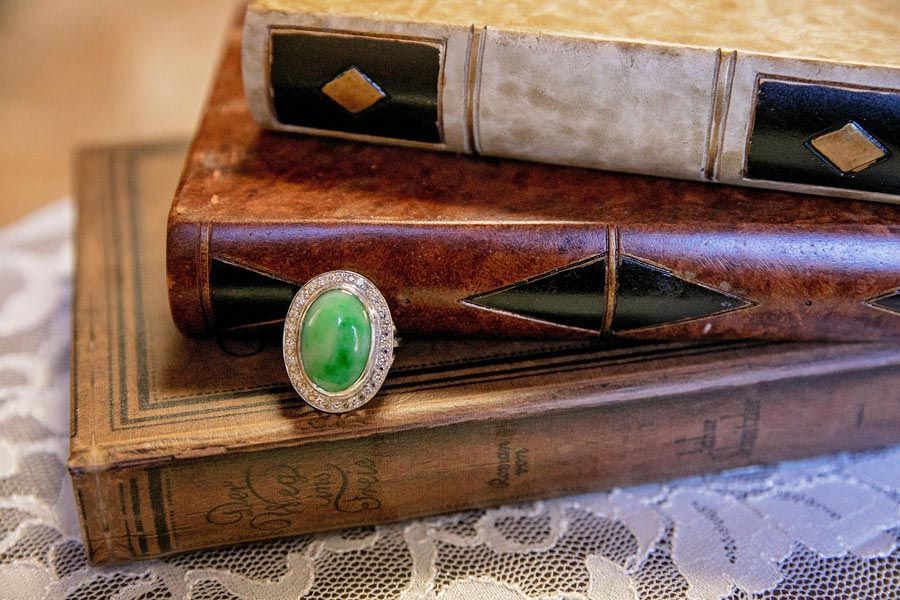 Green opal ring sitting on three decorative books stacked on lace, with an ornate green ring resting on top.