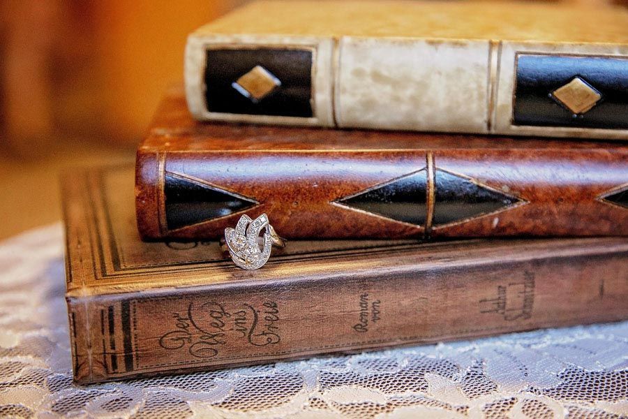 Diamond ring sitting on stacked vintage leather-bound books on a lace-covered surface