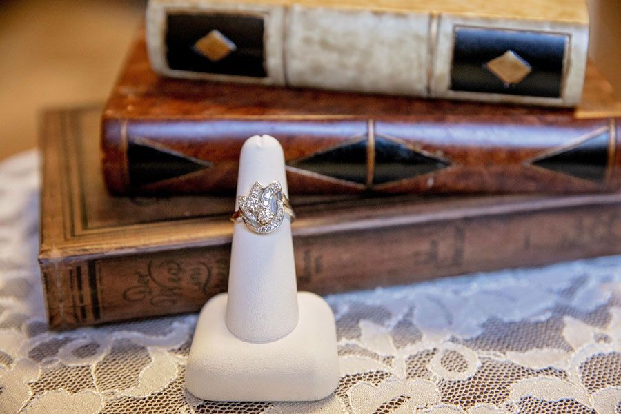 Gold diamond ring on white display stand in front of stacked wooden boxes on lace fabric.