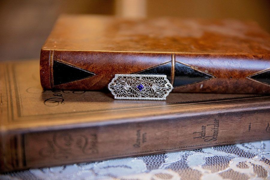 Two stacked vintage books with ornate brown leather covers and silver clasps on a lace tablecloth