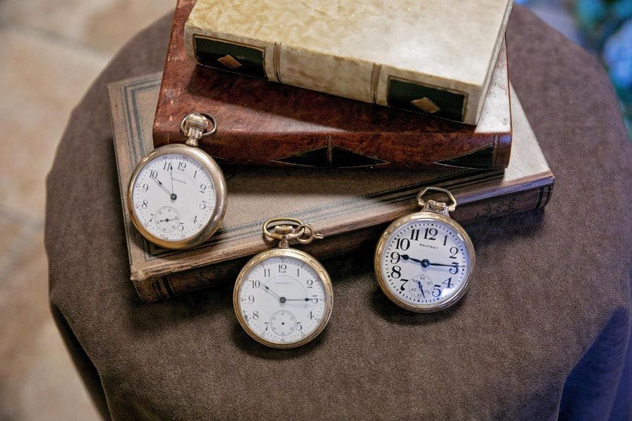 Three vintage pocket watches on stacked books with a brown cloth background