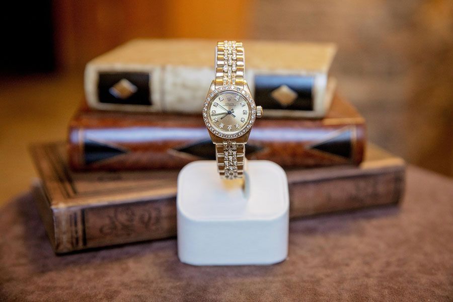 Gold wristwatch on a white stand with wooden boxes in the background