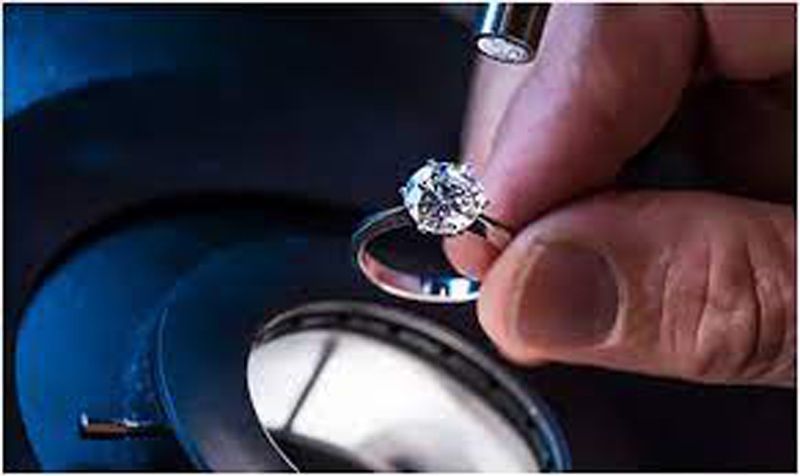 Hand holding a diamond under a jeweler’s loupe on a blue inspection surface