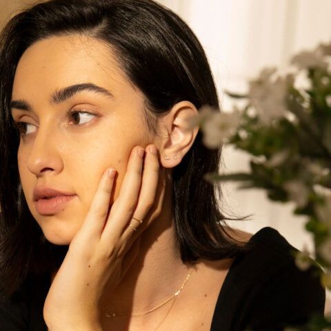 Close-up of a woman with dark hair touching her cheek in warm indoor light