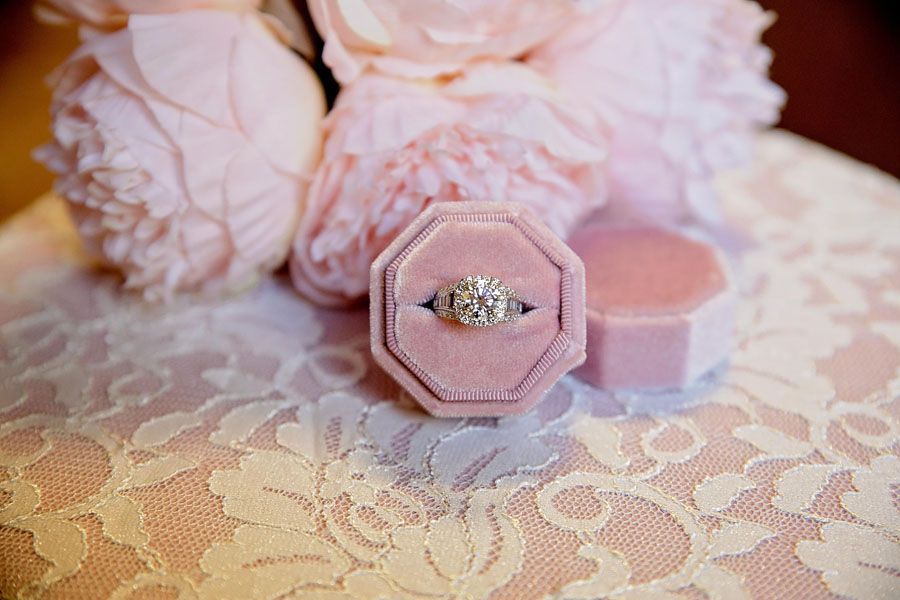 Pink ring box with diamond ring on lace, surrounded by soft pink flowers