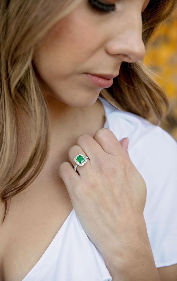 Woman in white blouse holding a hand near her collar, wearing a green gemstone ring.