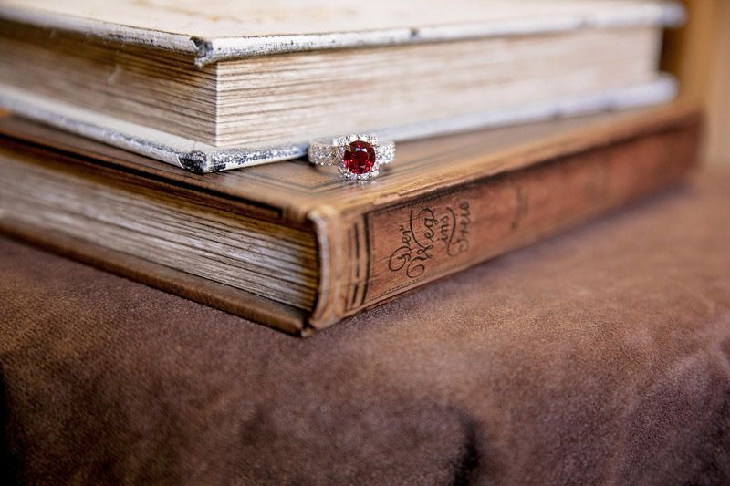 Two stacked old books with worn pages and a red gemstone ring on a brown velvet surface