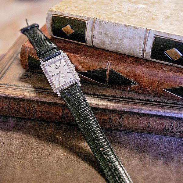 Green wristwatch on stacked leather-bound books with geometric inlays.