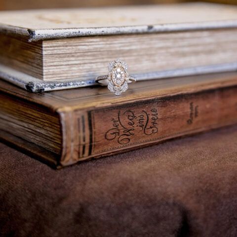 Stack of vintage books with a decorative ring on top, resting on a brown fabric surface