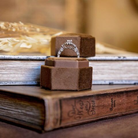 Wedding rings on a box resting atop stacked books, with warm blurred lights in the background