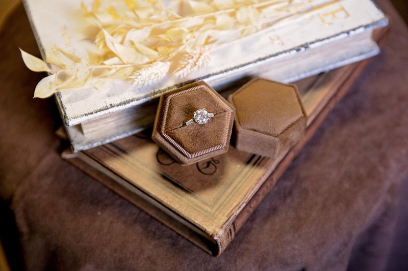 Octagonal wooden decorative jewelry box containing a diamond ring on a stacked wood tray with a white flower arrangement