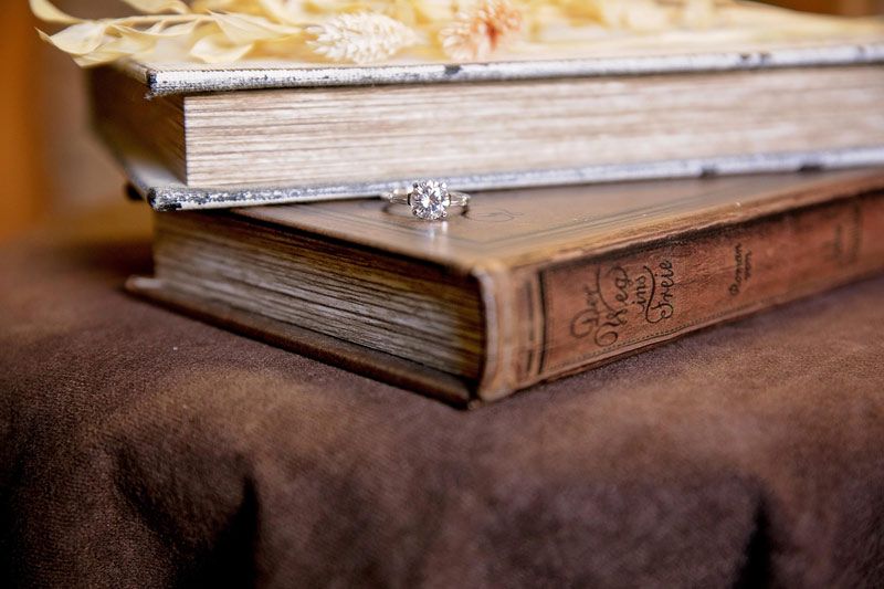Diamond engagement ring sitting on two stacked vintage books on a brown fabric surface