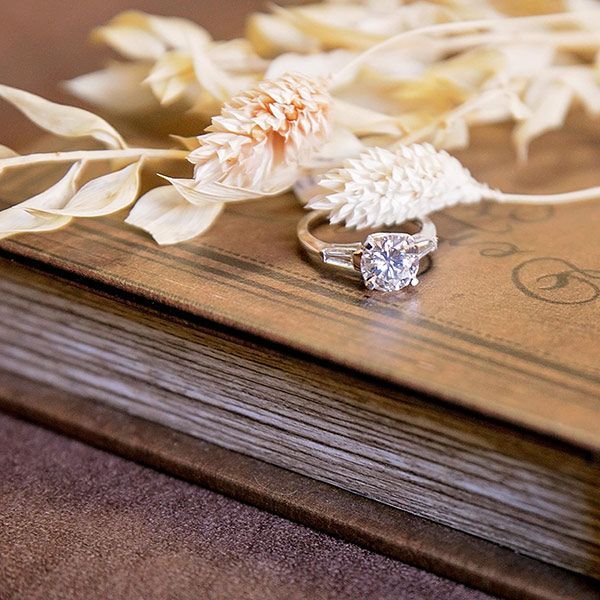 White flowers and a diamond ring on a wooden book with a brown fabric background