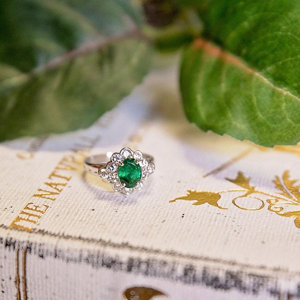 Silver ring with green gemstone on a decorative book, framed by soft green leaves