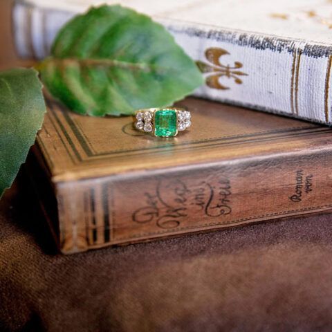 Emerald ring on stacked vintage books with a green leaf in the foreground
