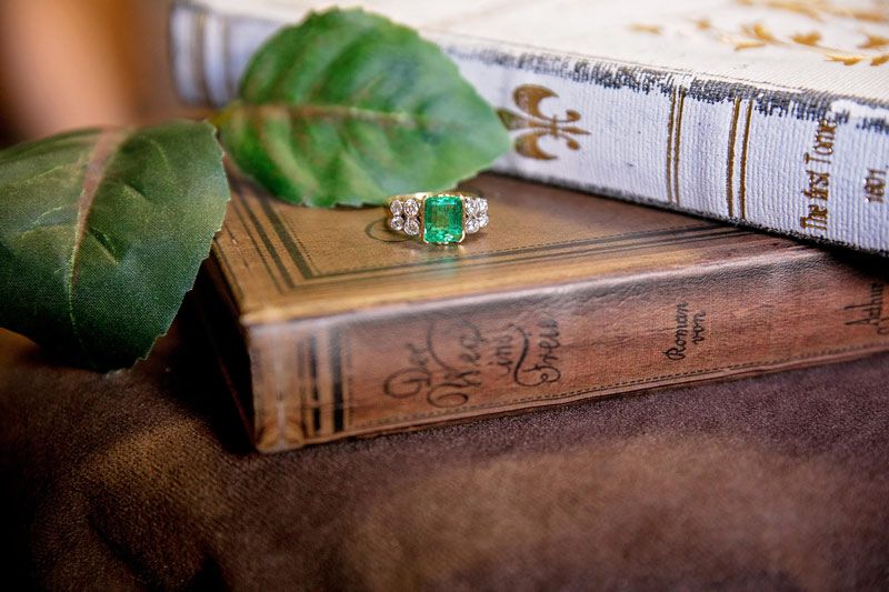 Green gemstone ring resting on stacked vintage books beside a leafy branch