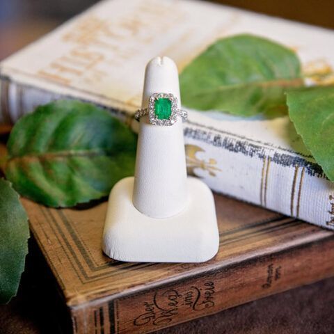 Emerald ring on a white display stand beside green leaves and vintage books