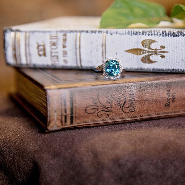 Two stacked vintage books with a turquoise ring on top, resting on a brown fabric surface.