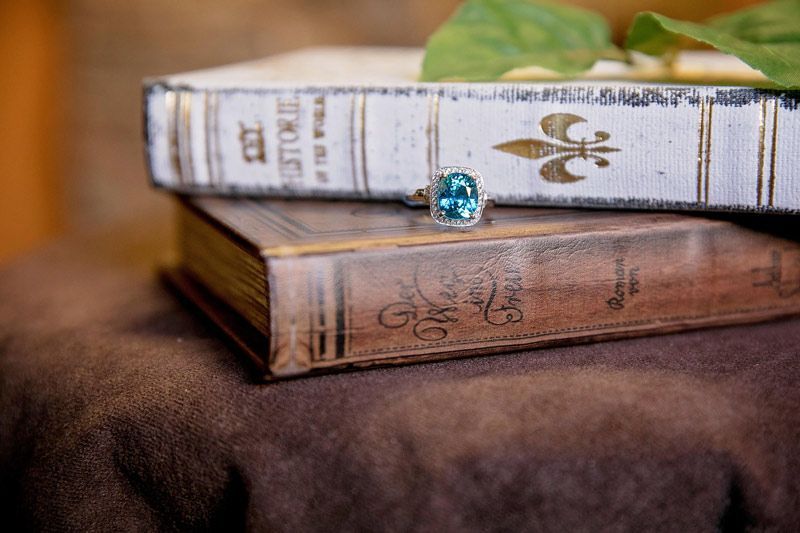 Two stacked decorative books with a blue gem on a brown cloth table, green leaf in background