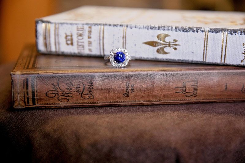 Stacked vintage books with a blue ring on top, resting on a leather surface
