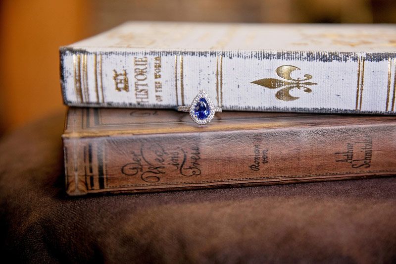 Two vintage books stacked on a brown surface, one white with a blue jeweled clasp and one brown leather-bound.