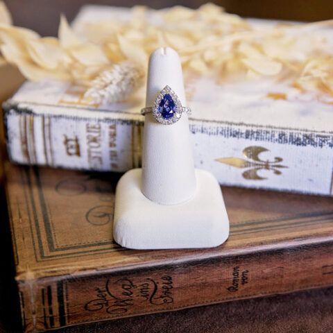 White ring stand with a blue gemstone ring on stacked vintage books and dried flowers