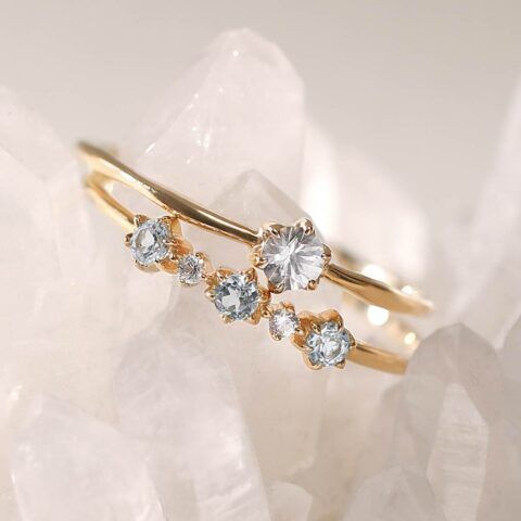 Gold ring with clear gemstones arranged in a curved floral design on a pale crystal background