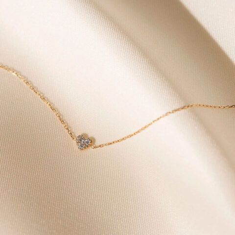 Delicate gold necklace with a small pendant on soft beige fabric.