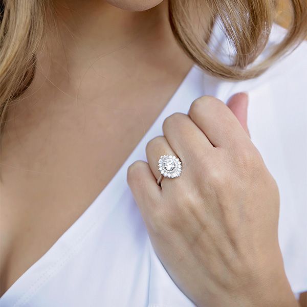 Close-up of a hand wearing a large diamond ring against a white dress