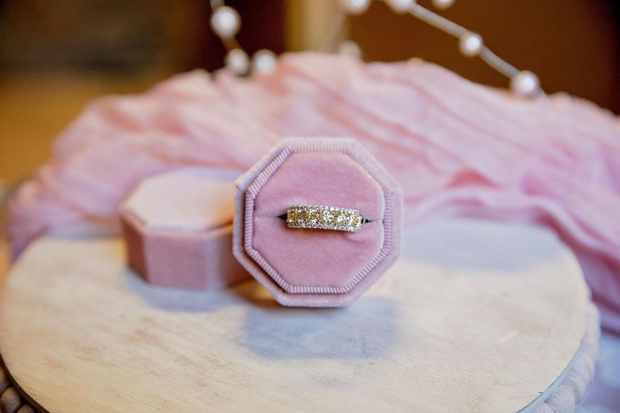 Pink octagonal velvet ring box with a gold diamond ring on a soft surface