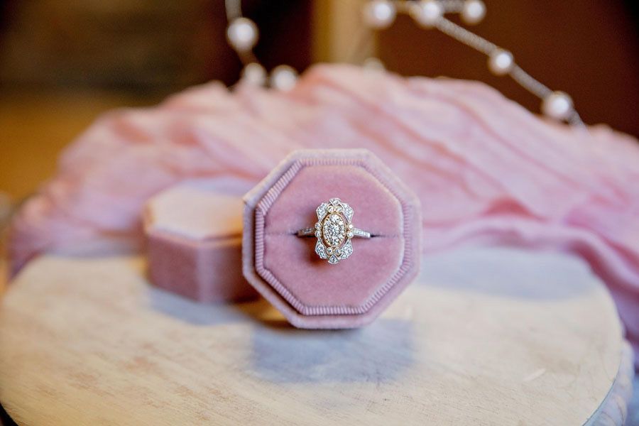 Pink velvet ring box with diamond ring on a round wooden table, with a soft pink background