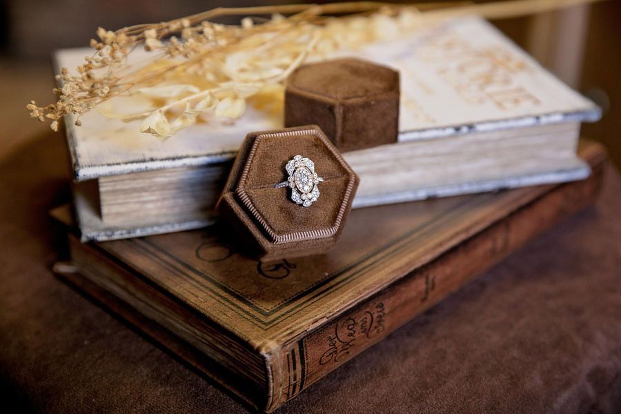 Stacked vintage books with a hexagonal wooden ring box on top, featuring a jeweled ring