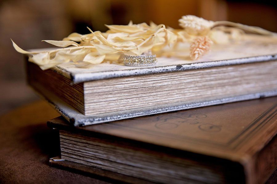Stack of rustic hardcover books with dried flowers and a diamond ring on top