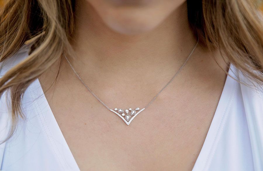 Close-up of a silver V-shaped necklace with small stones on a white blouse.