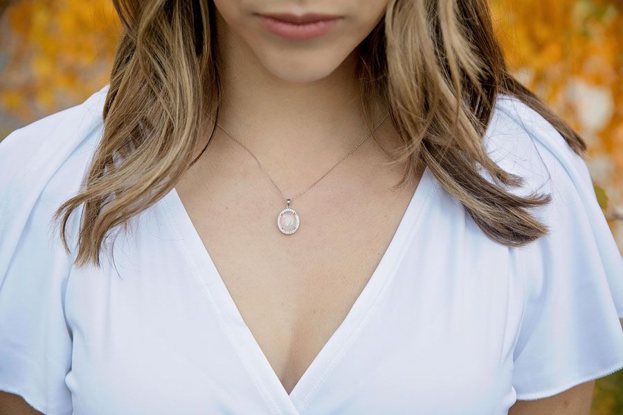 Woman in a white V-neck dress wearing a silver pendant necklace outdoors in autumn.