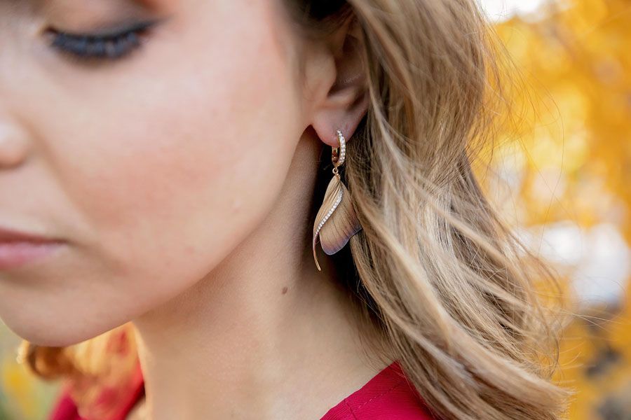 Close-up of a woman wearing teardrop earrings, with blonde hair and a blurred autumn background