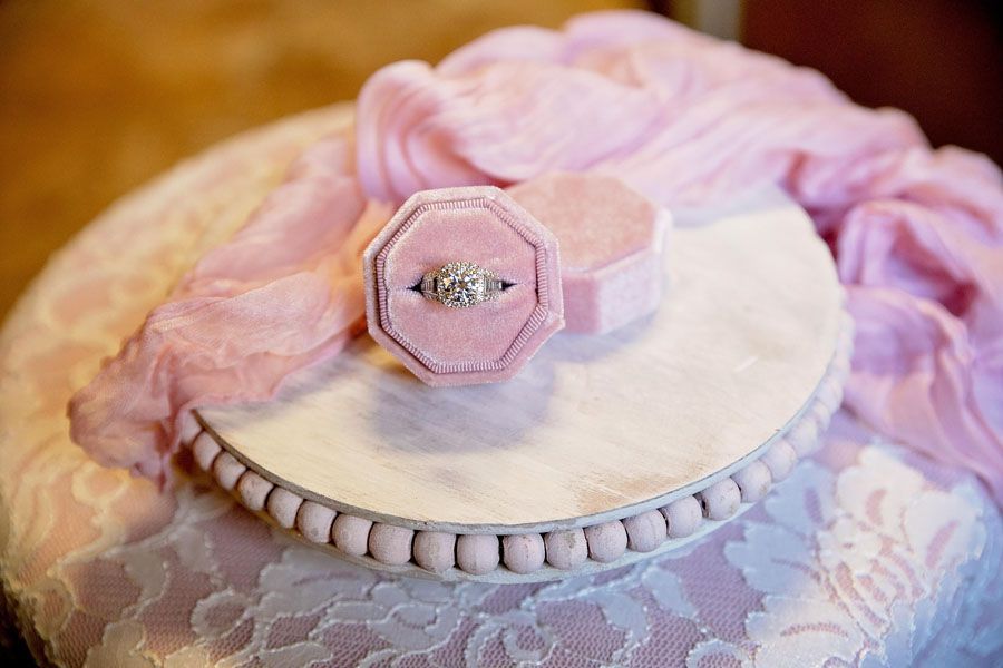 Pink lace gift box with white round lid and a hexagonal diamond ring on a decorative cushion