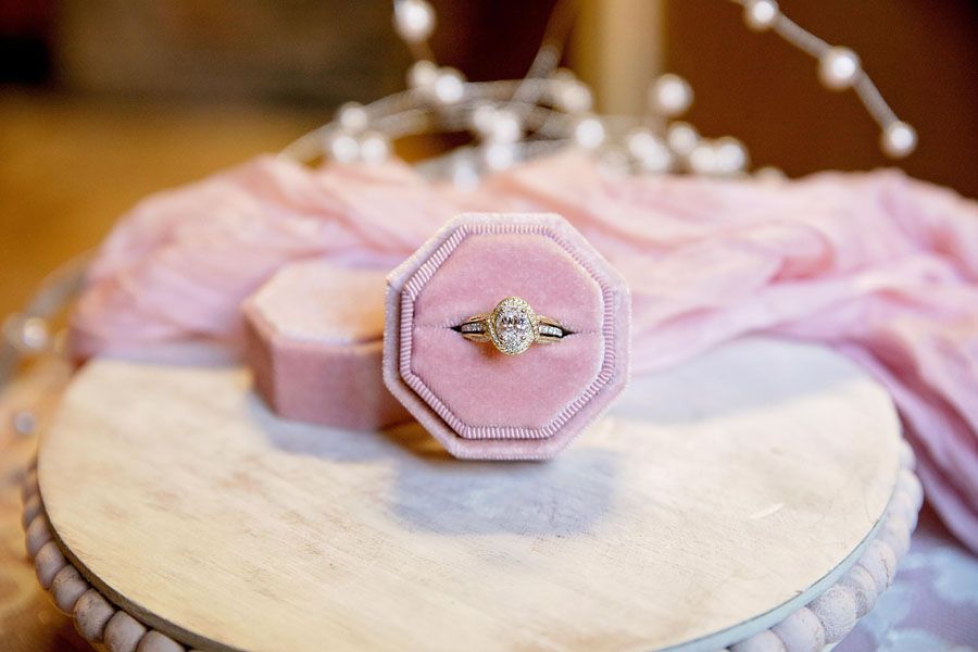 Pink velvet ring box with diamond ring on a round marble pedestal with soft pink tulle backdrop