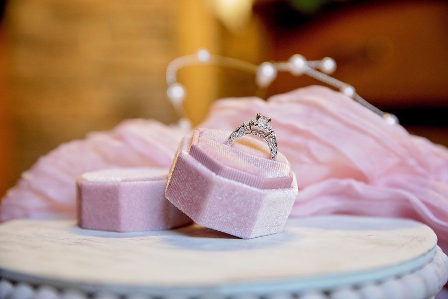 Pink velvet ring box with a silver ring, resting on a white cake stand or table