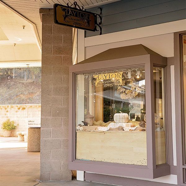 Storefront window display with jewelry and a hanging sign under a covered walkway